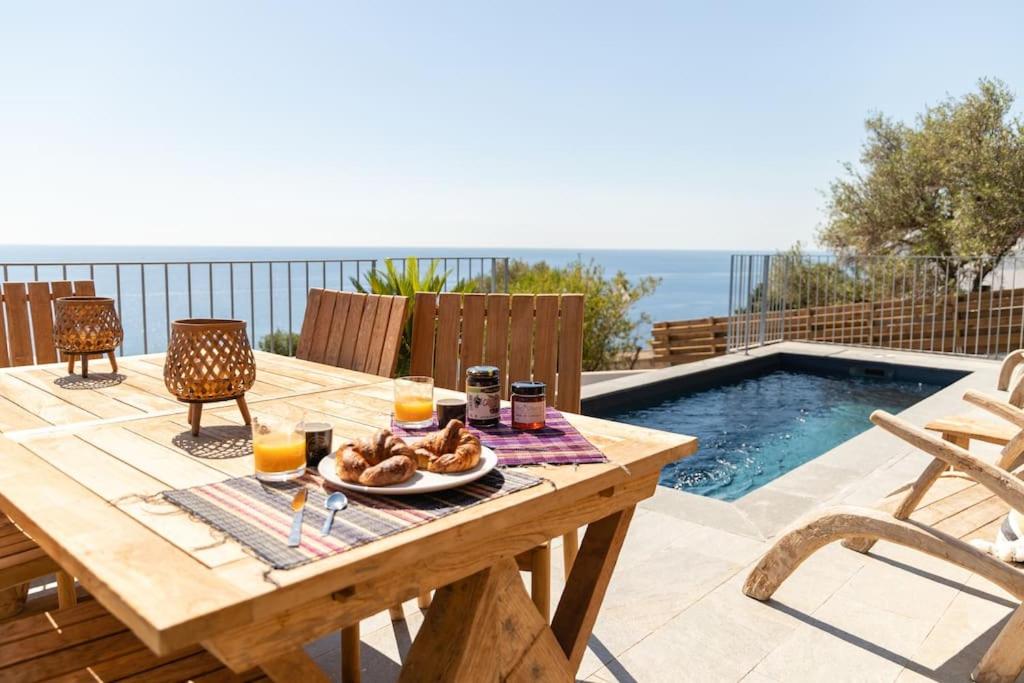 ein Holztisch mit einem Teller Essen auf dem Tisch neben einem Pool in der Unterkunft Belle villa vue mer- Erbalunga à 2 pas de la plage in Brando