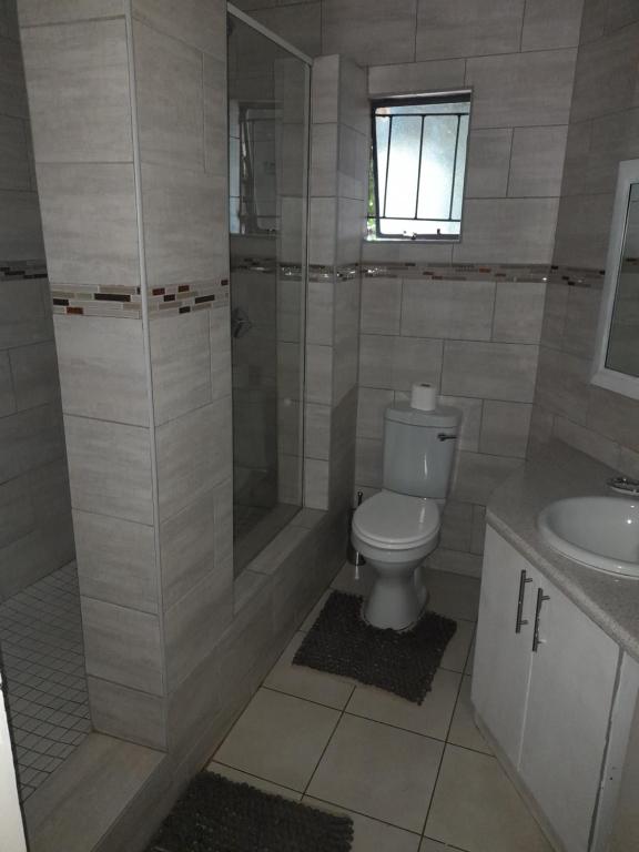 a bathroom with a shower and a toilet and a sink at Charis Guesthouse in Hartswater
