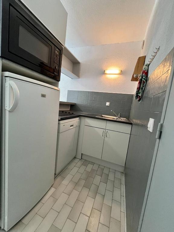 une petite cuisine avec des armoires blanches et un micro-ondes dans l'établissement STUDIO CABINE 4 PERSONNES AVEC TERRASSE ET PLACE DE PARKING PRIVATIVE, au Grau-du-Roi