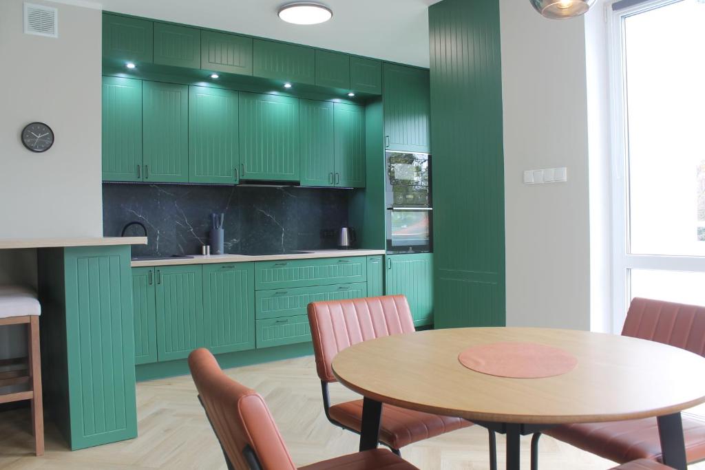 une cuisine avec des armoires vertes, une table et des chaises dans l'établissement Apartament przy Zodiaku, à Mrągowo