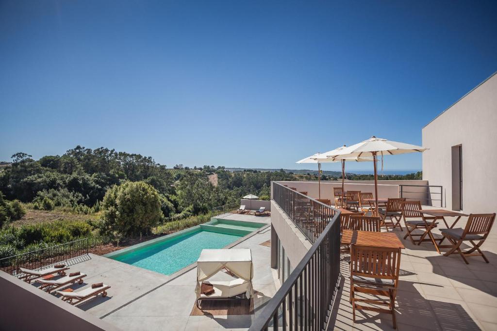 uma varanda com uma piscina e cadeiras e um guarda-sol em Vale d'Azenha Hotel Rural & Residences em Alcobaça