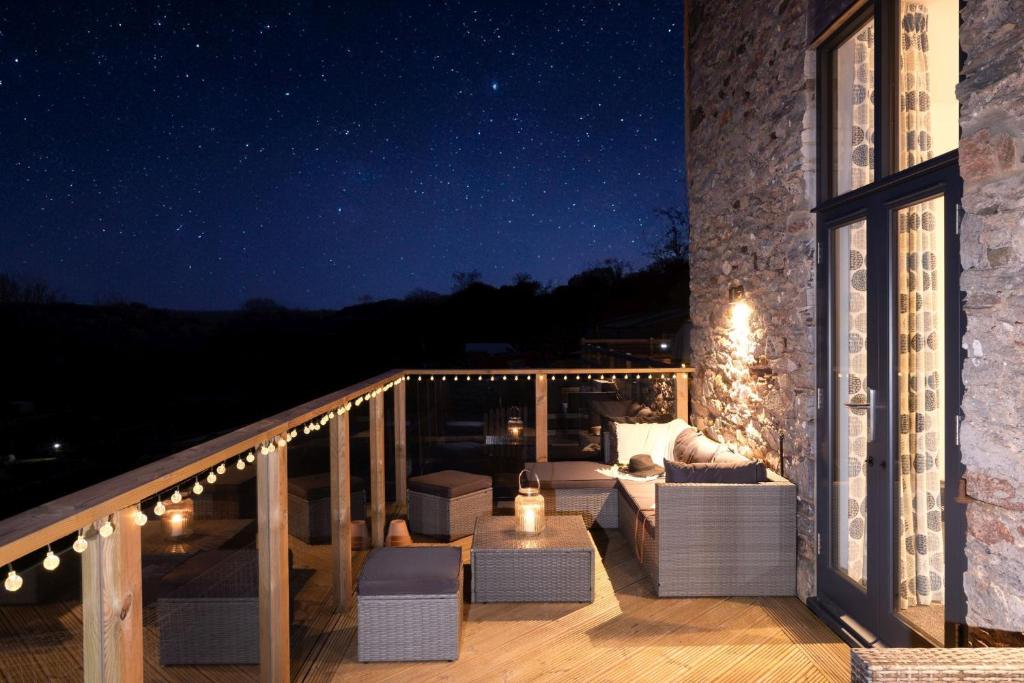 a balcony with a couch and chairs at night at The Linhay, Higher Yalberton Farm in Paignton