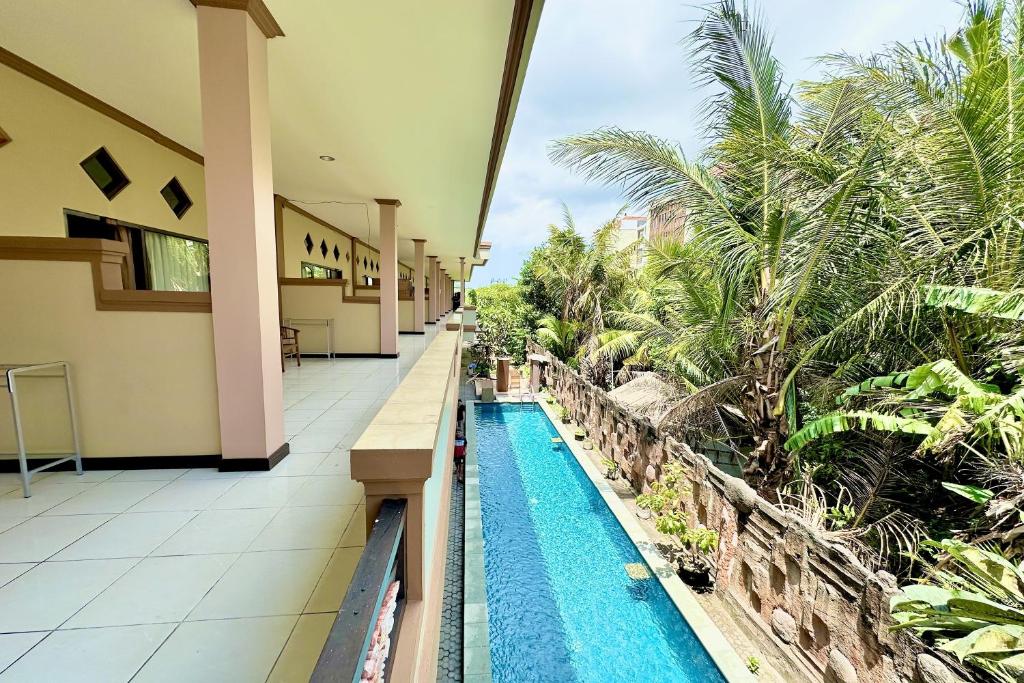 a resort with a swimming pool and palm trees at Taxa Raya Guest House in Legian