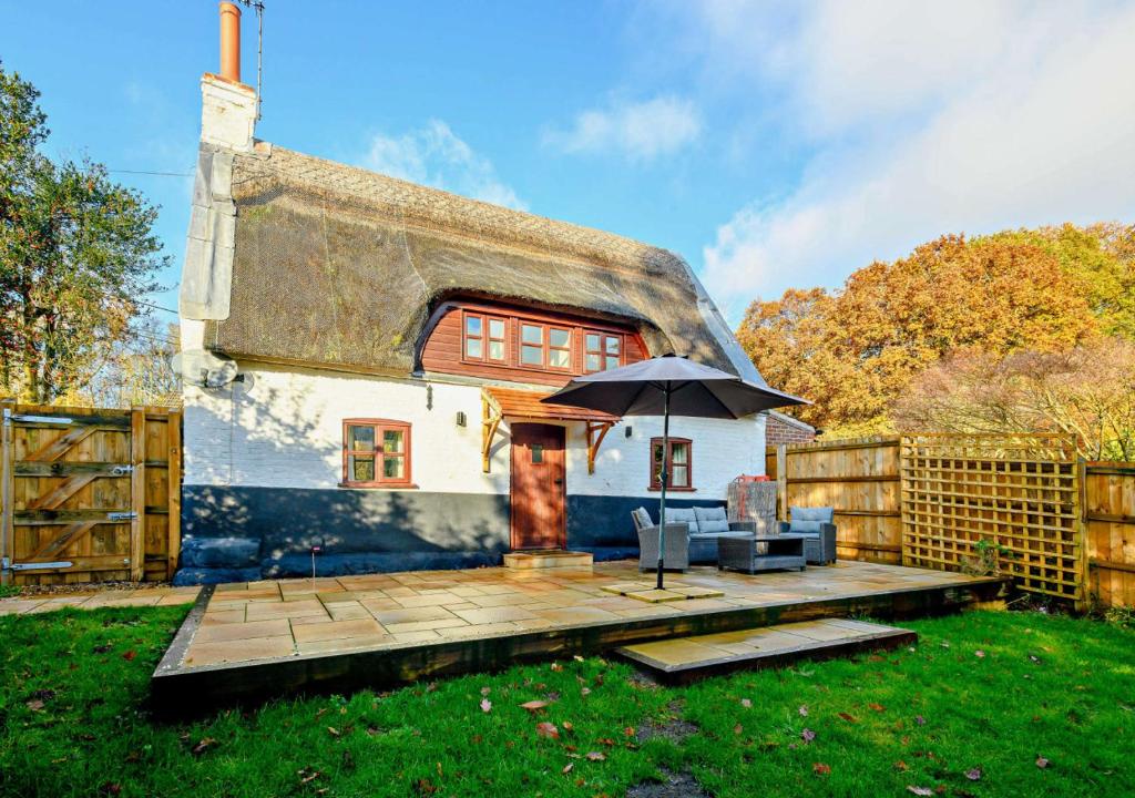 a cottage with an umbrella and a wooden deck at Holly Cottage in Panxworth