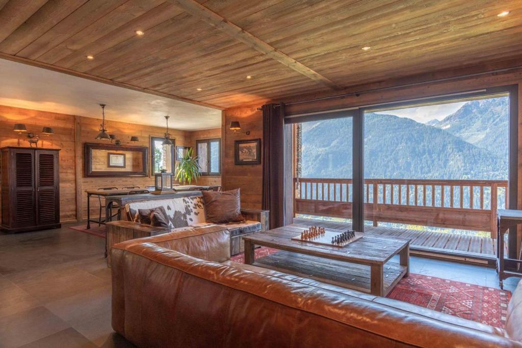 a living room with a leather couch and a large window at Chalet Apalosa - Montvalezan, La Rosière in Montvalezan