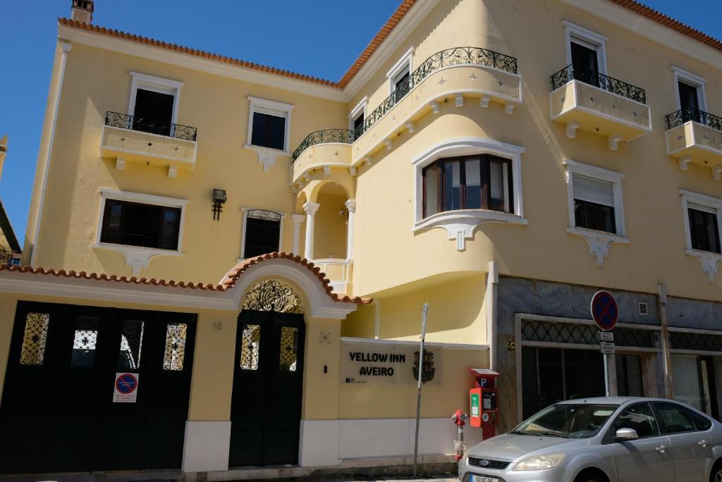 Un edificio amarillo con un coche aparcado delante. en Yellow Inn Aveiro, en Aveiro