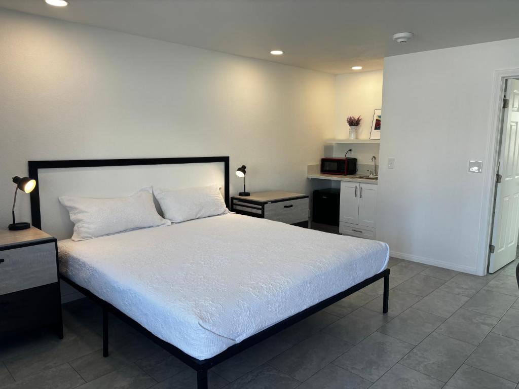 a bedroom with a bed with white sheets and a kitchen at Boulder City Inn in Boulder City