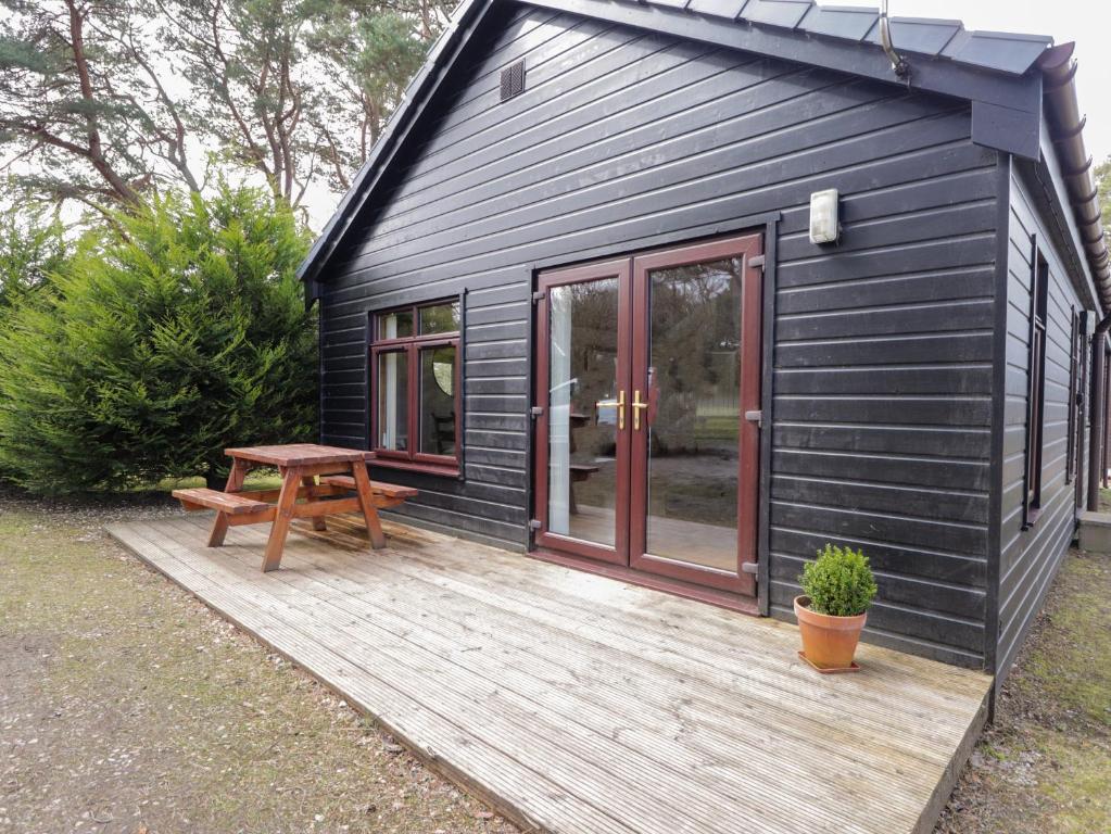 a black house with a picnic table on a wooden deck at Chalet C in Dornoch