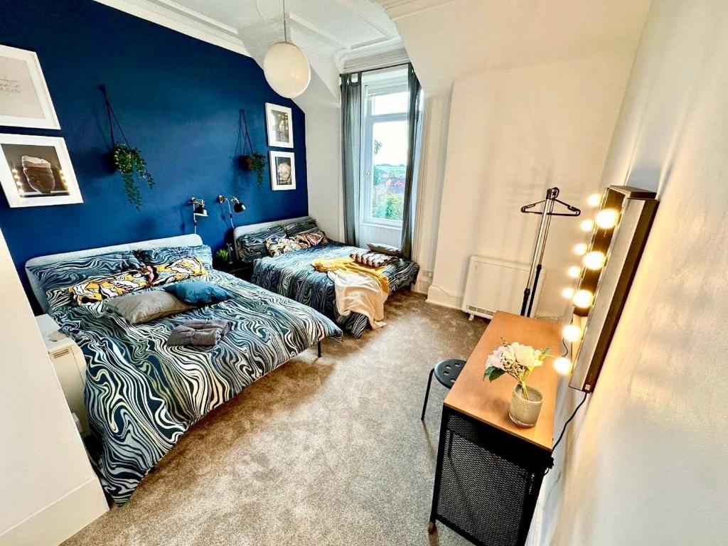 a blue room with two beds and a table at Cosy stylish Dumbarton flat in Dumbarton