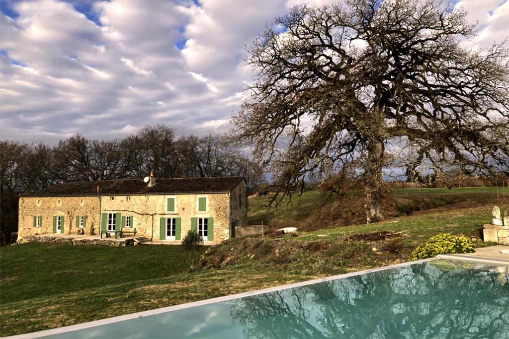 une grande maison en pierre avec un arbre et une piscine dans l'établissement Chambre spacieuse dans très belle batisse en pierre restaurée et isolée dans un écrin de nature, à Pellegrue