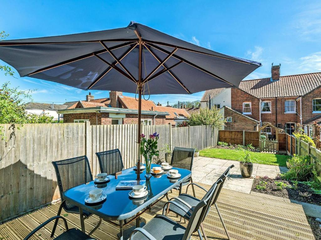 a blue table with chairs and an umbrella on a patio at Forsythia House in Overstrand