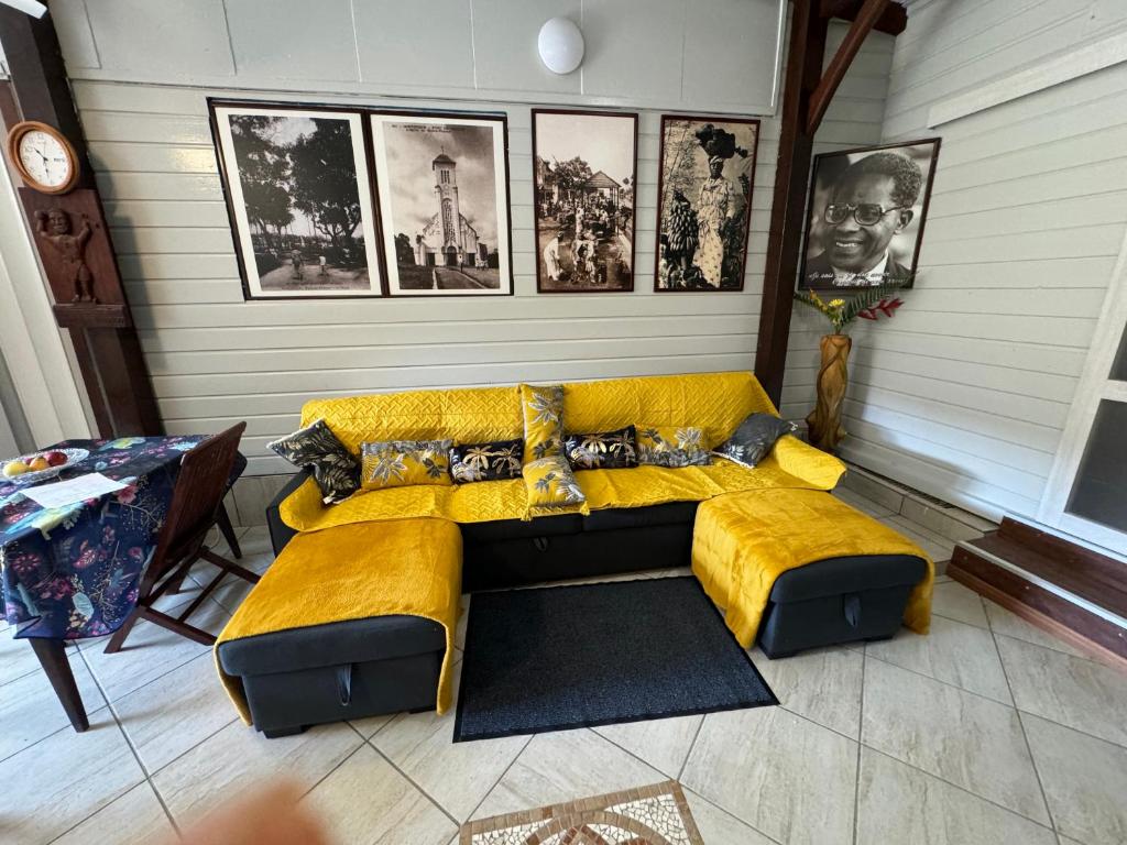 un sofá amarillo en una habitación con fotos en la pared en residence caramboles en Fort-de-France