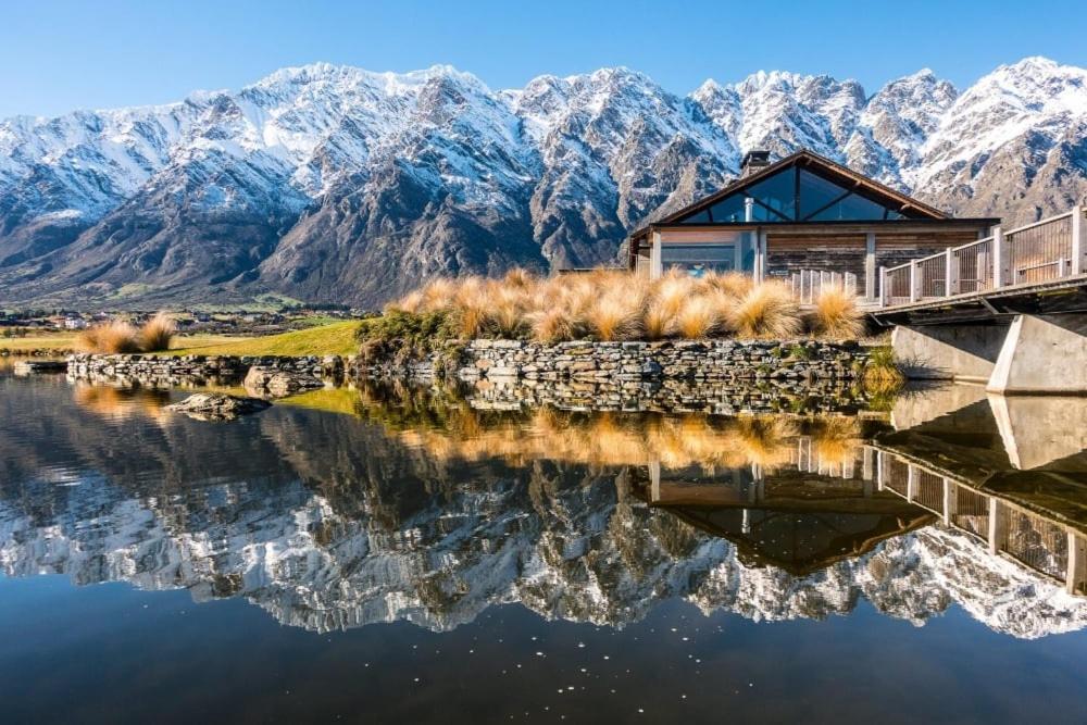 a house on a lake with mountains in the background at Luxury Alpine Retreat with a hot tub in Frankton