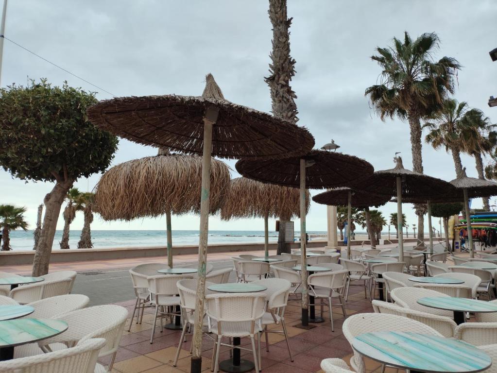 eine Reihe von Tischen und Stühlen mit Sonnenschirmen am Strand in der Unterkunft Alicante El Campello 1º línea de playa in El Campello