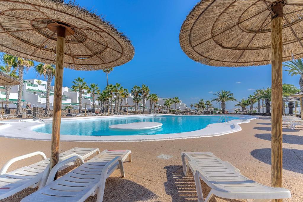 basen z leżakami i parasolami na plaży w obiekcie Bonito apartamento reformado en Las Coronas w Costa Teguise