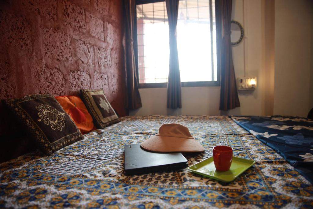 Sombrero y ordenador portátil en una cama con ventana en Arpita FarmStay, en Malvan