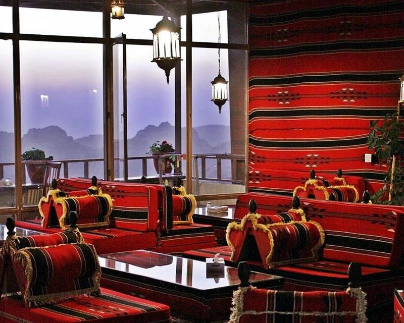 a room with red chairs and a balcony with mountains at Rocky Mountain Hotel in Wadi Musa