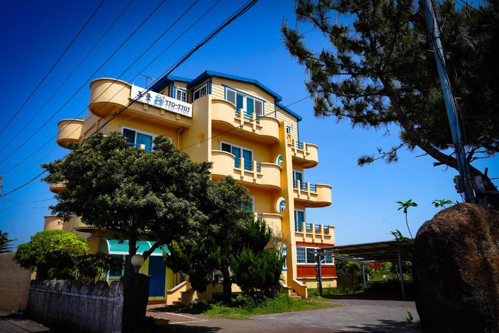 a yellow building with blue windows on a street at ttottot Jeju Backpackers in Seogwipo