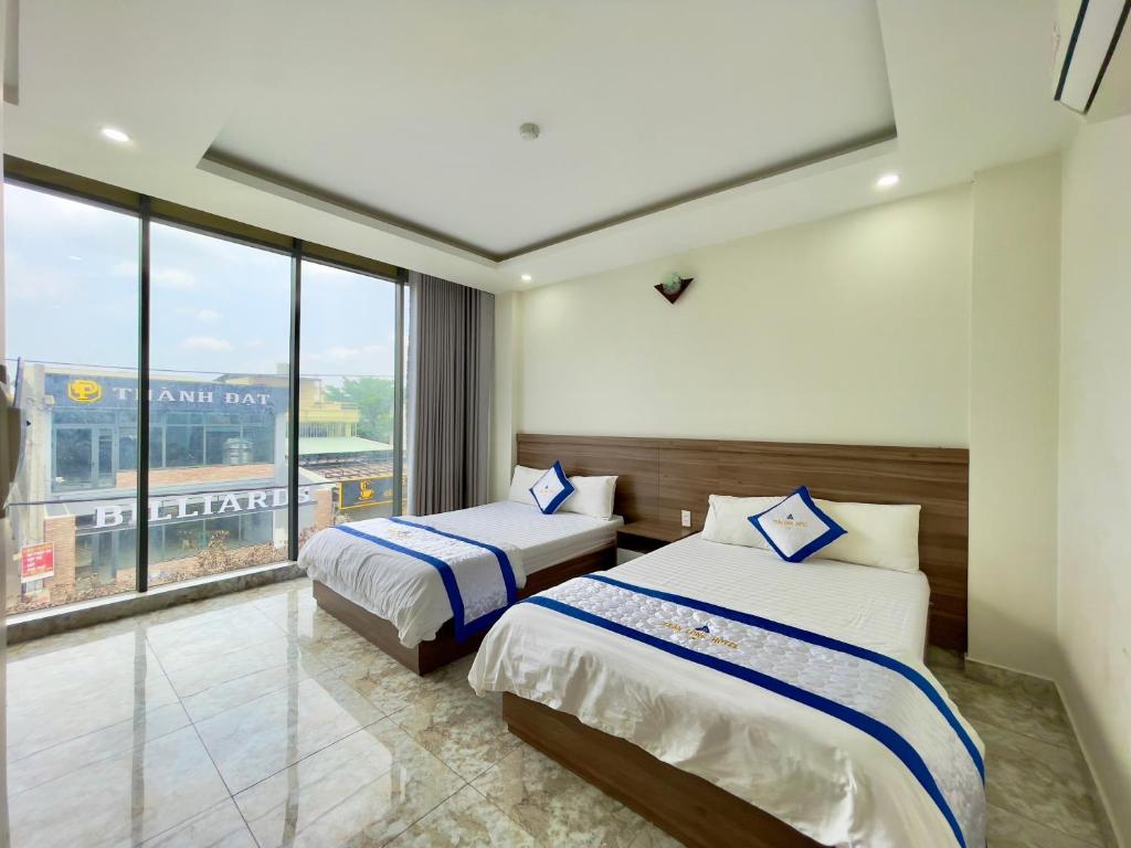 two beds in a room with a large window at Khách Sạn TRẦN LONG in Ho Chi Minh City