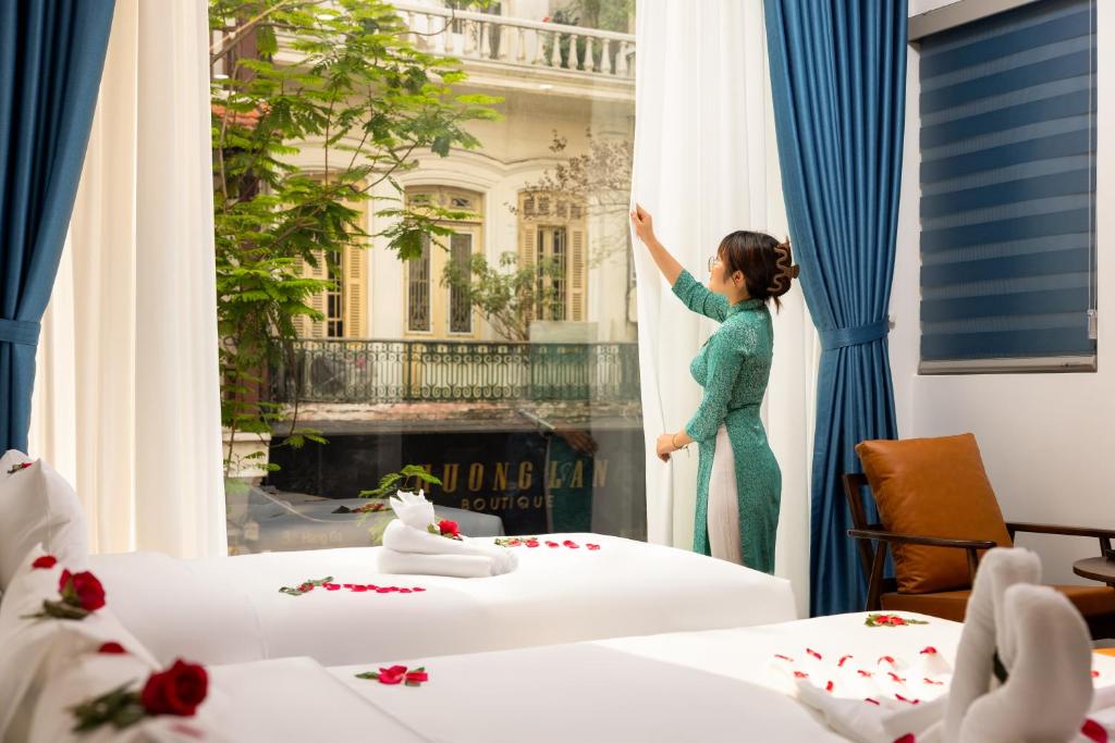 uma mulher está a olhar pela janela de um quarto de hotel em Casa Valentina Hanoi Hotel em Hanói