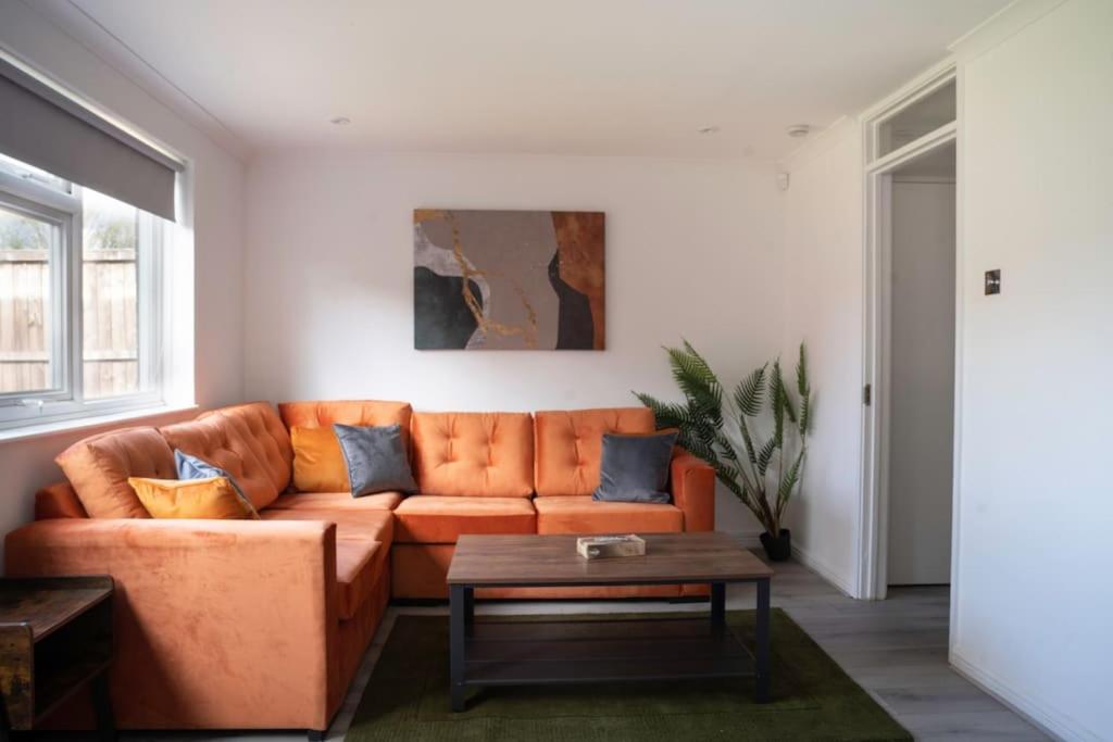 an orange couch in a living room with a table at Modern 3 Bedroom house in Finchley in Totteridge