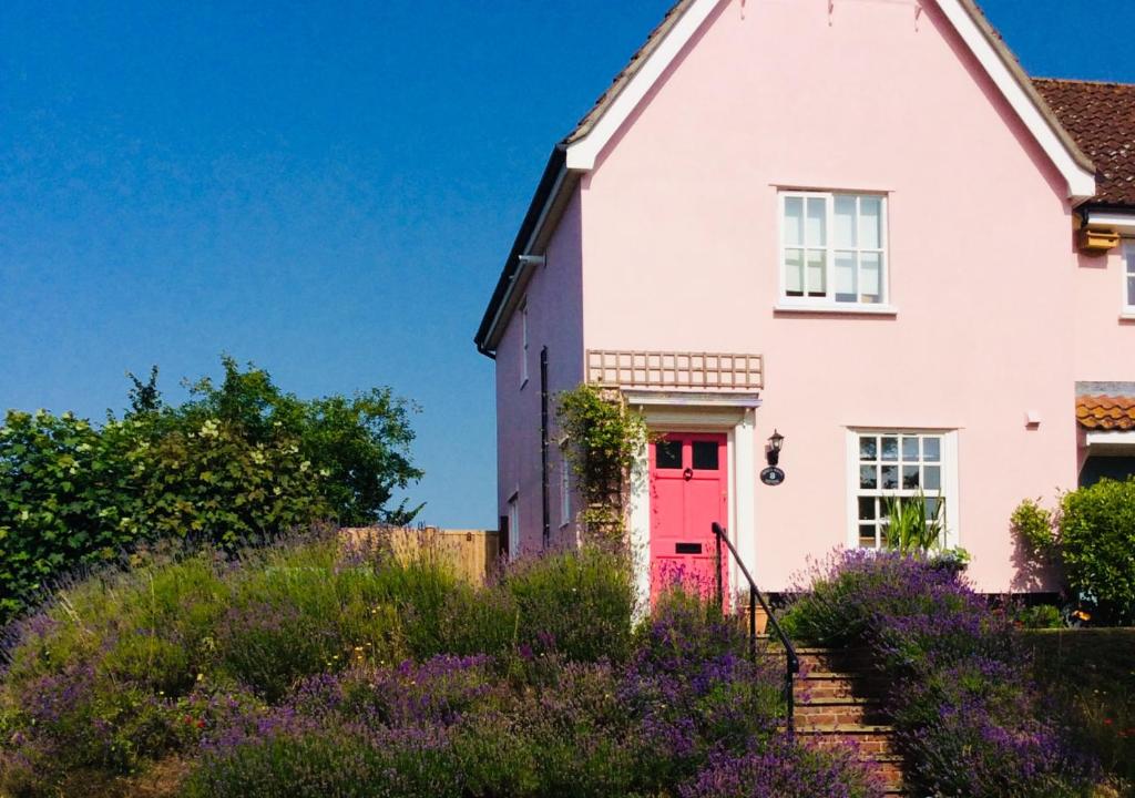 黑爾斯沃思的住宿－Honeysuckle，白色的房子,有红色的门和紫色的鲜花
