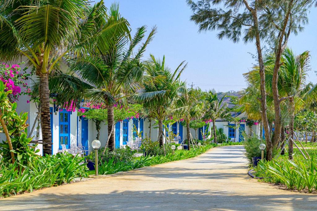 uma estrada ladeada por palmeiras e edifícios azuis em KIGI Beach Resort em Phan Thiet