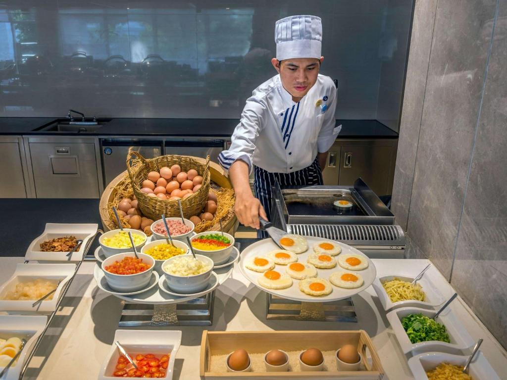 a chef standing in a kitchen preparing food at Novotel Phuket City Phokeethra in Phuket Town