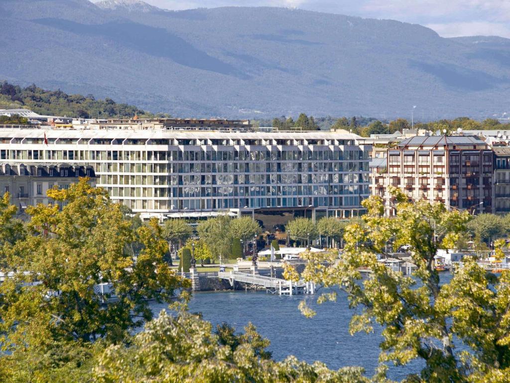 - un grand bâtiment à côté d'une étendue d'eau dans l'établissement Fairmont Grand Hotel Geneva, à Genève