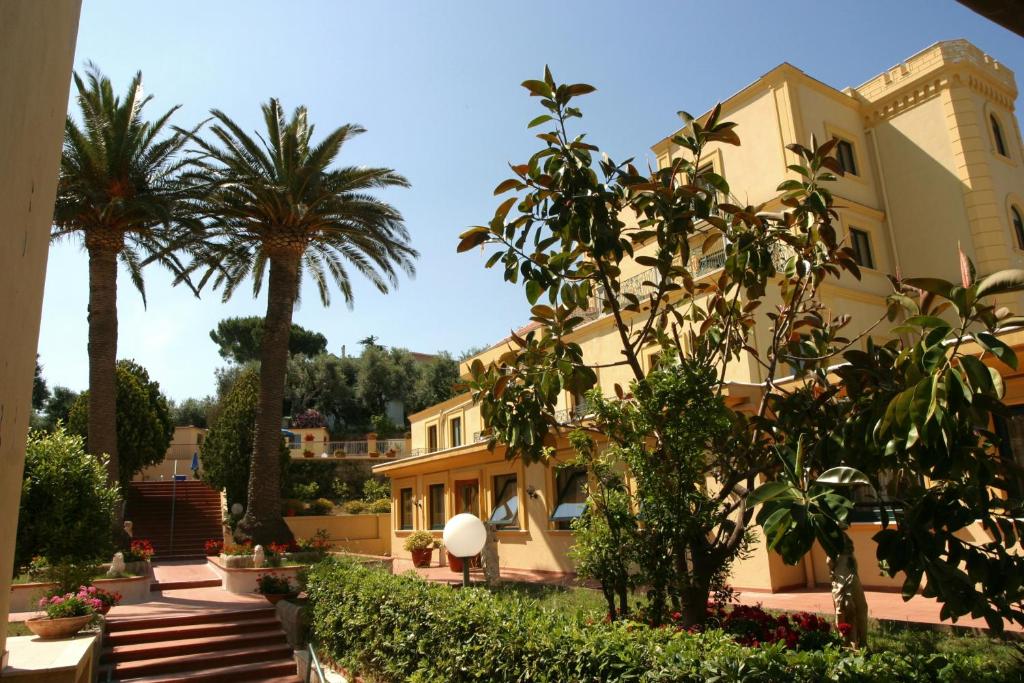 a large yellow building with palm trees and bushes at Hotel Villa Igea in Sorrento