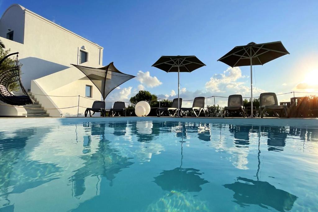 a swimming pool with chairs and umbrellas at Hermoso Luxury Suites in Monolithos