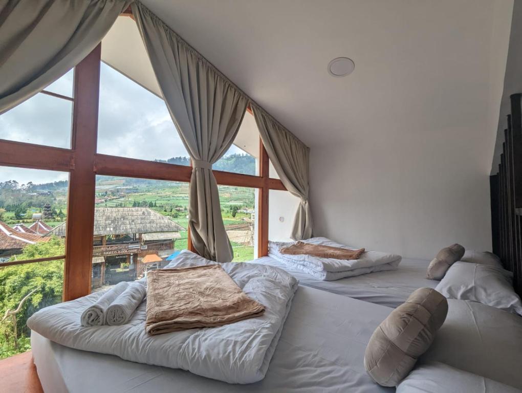 two beds in a room with a large window at Cottage Linggayoni Dieng 1 in Dieng