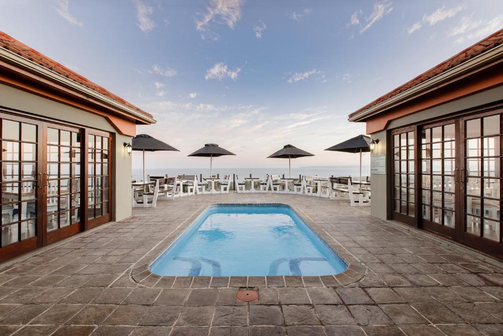 a swimming pool on a patio with chairs and umbrellas at Garden Route Ilita Lodge in Great Brak River