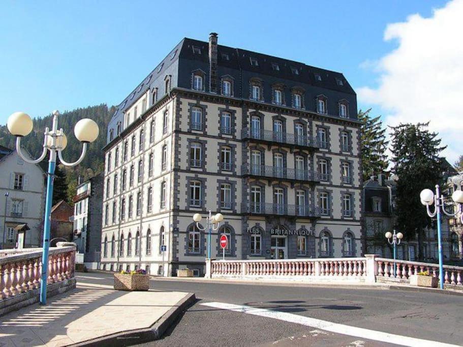 un grand bâtiment blanc avec un pont devant lui dans l'établissement Résidence Les Iles Britanniques, à La Bourboule