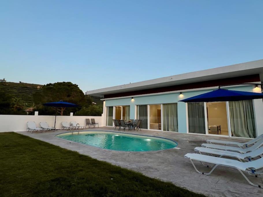 a pool with chairs and umbrellas next to a house at Villa Marinos in Kalamaki