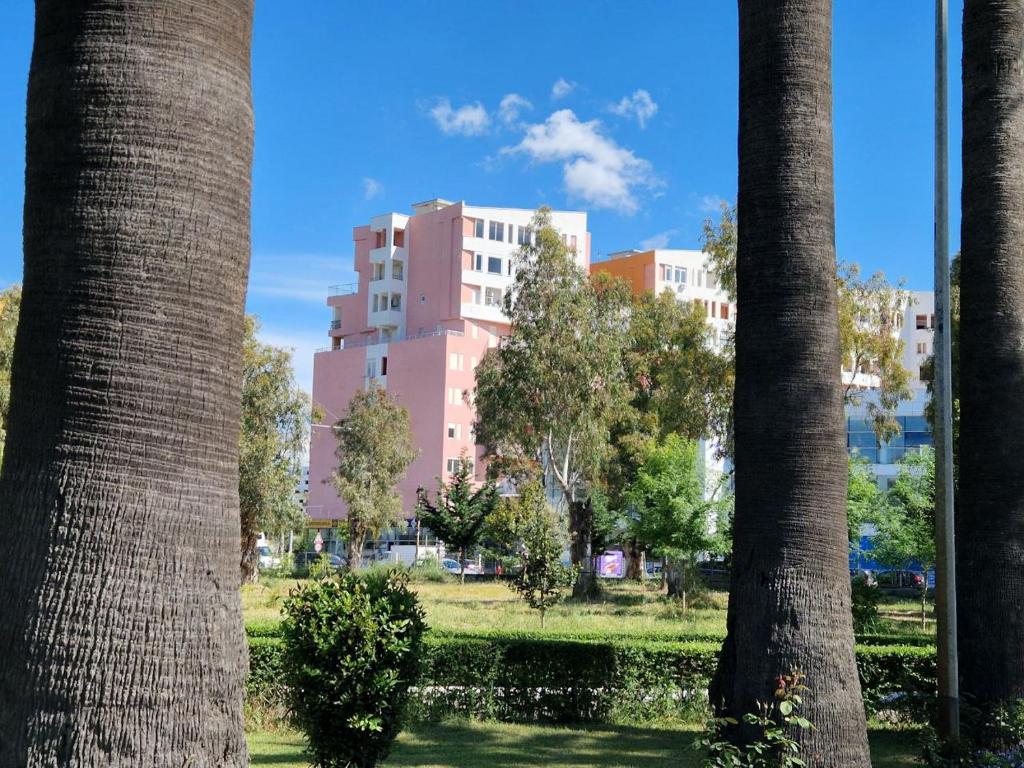 um edifício rosa num parque com palmeiras em Tropical Apartment em Durrës