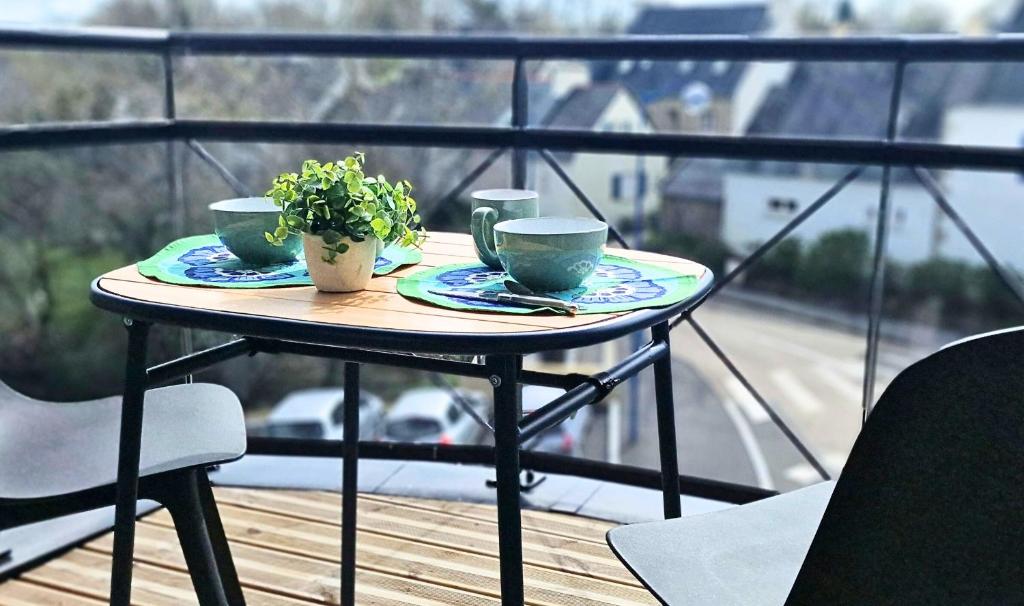 une table avec deux tasses et une plante sur un balcon dans l'établissement Appartement moderne, hyper-centre, 2km des plages, à Fouesnant