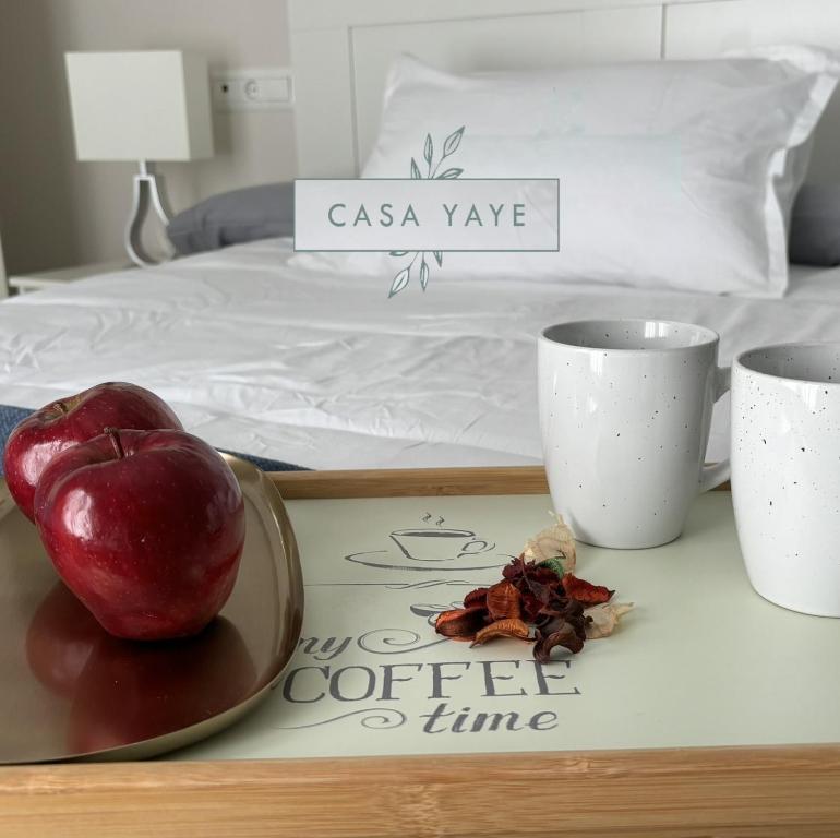 una bandeja con una manzana y dos tazas en una cama en Casa Yaye Aguabajo, en Écija
