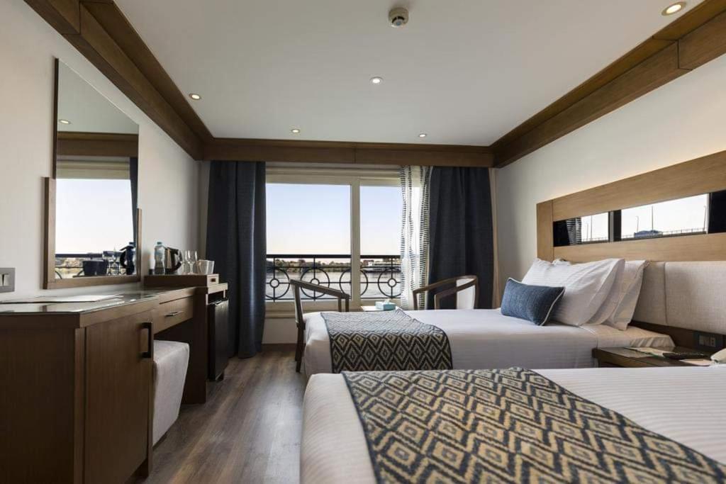 a hotel room with two beds and a bathroom with a view at Kiara Nile Cruise every Saturday, Monday and Thursday from Luxor in Jazīrat al ‘Awwāmīyah