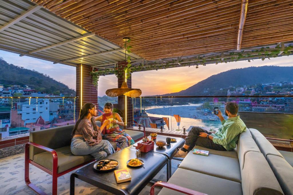 un grupo de personas sentadas en un balcón con vistas a la puesta de sol en The Hosteller Rishikesh, Ganges, en Rishīkesh