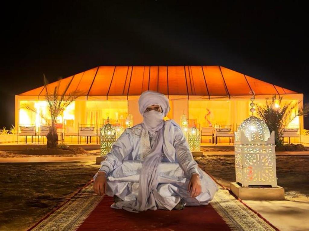 a person sitting on the ground in front of a building at Global Luxury Camp in Merzouga