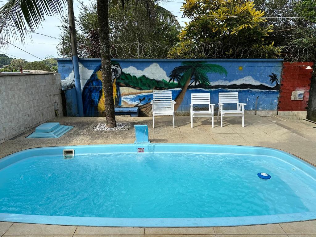 a blue swimming pool with two chairs and a mural at Aconchego da Vila in Mangaratiba