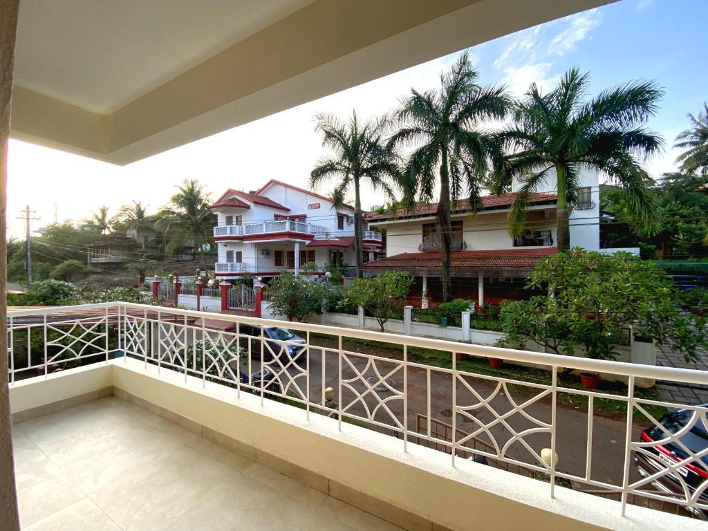 een balkon met uitzicht op een huis met palmbomen bij Quintara Serviced Apartments in North Goa in Porvorim