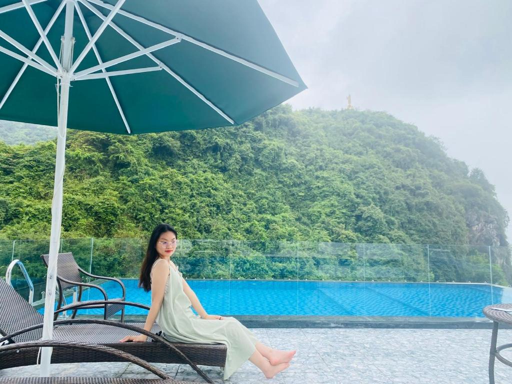 Una donna seduta su una sedia sotto un ombrello di Sand Hotel a Cat Ba