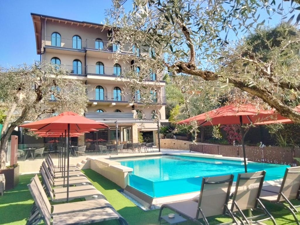 una piscina con sillas y sombrillas frente a un hotel en Hotel Al Caminetto WorldHotels Crafted Adults Only, en Torri del Benaco