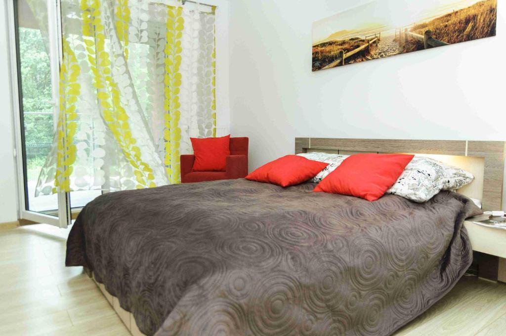 ein Schlafzimmer mit einem Bett mit roten Kissen und einem Stuhl in der Unterkunft Apartament Inez in Kołobrzeg