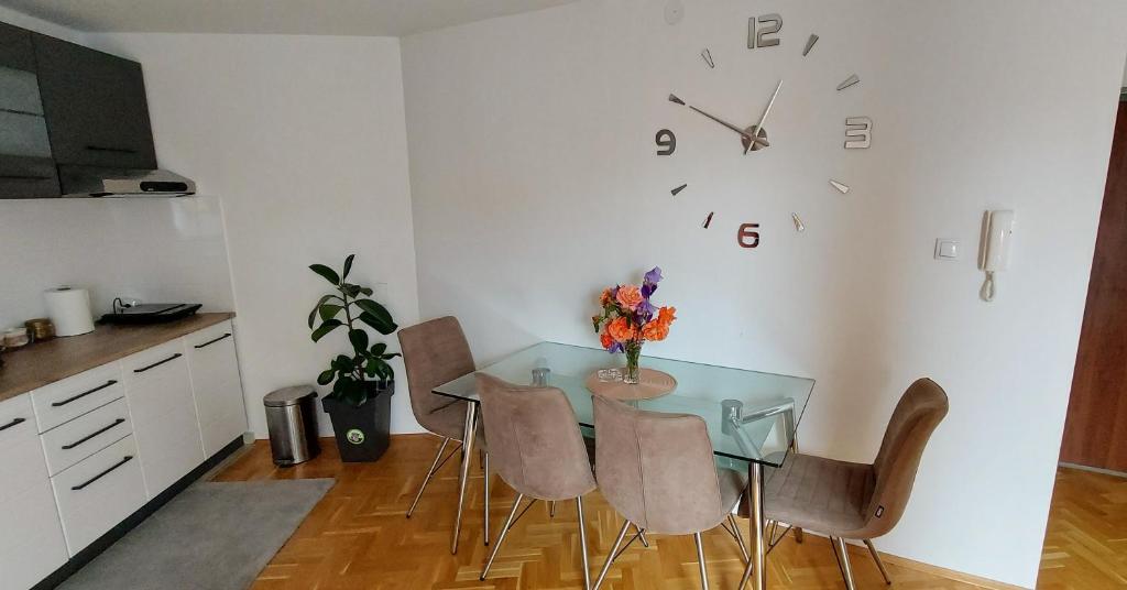 a dining room table with chairs and a clock on the wall at Apartman Panorama in Požarevac