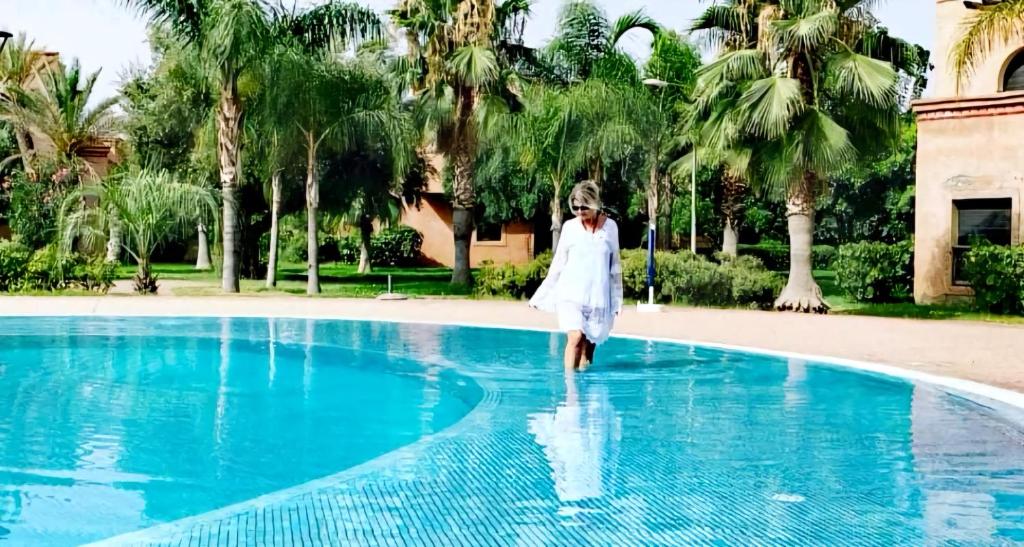 una mujer vestida de blanco entrando en una piscina en La Perle de l'Atlas by Golf Resort en Marrakech