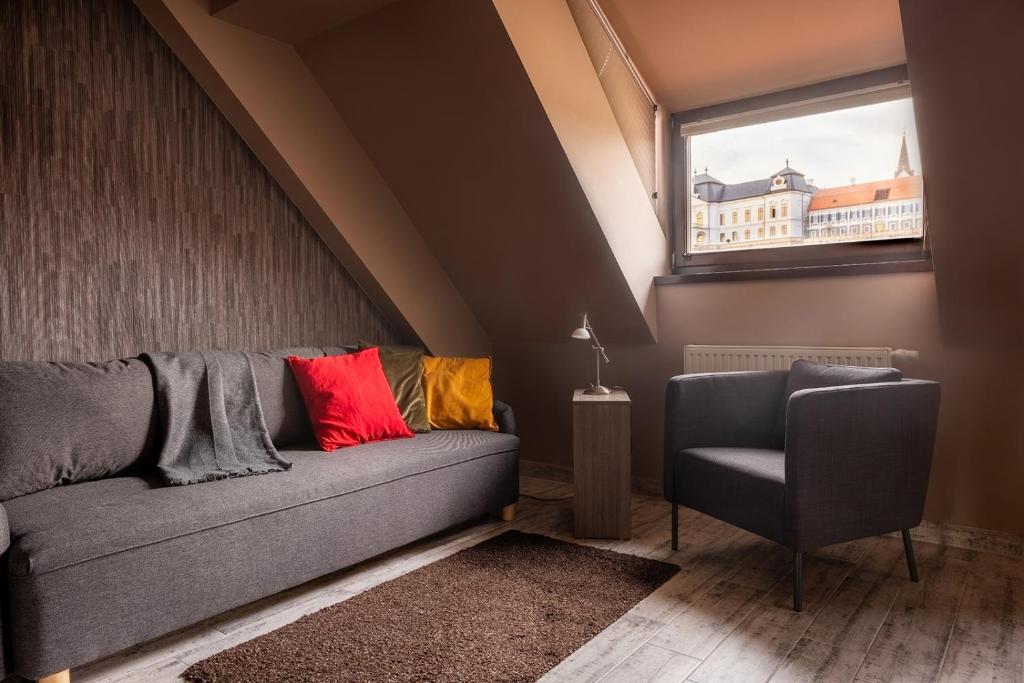 a couch and a chair in a room with a window at Laza napok apartman - 1 in Veszprém
