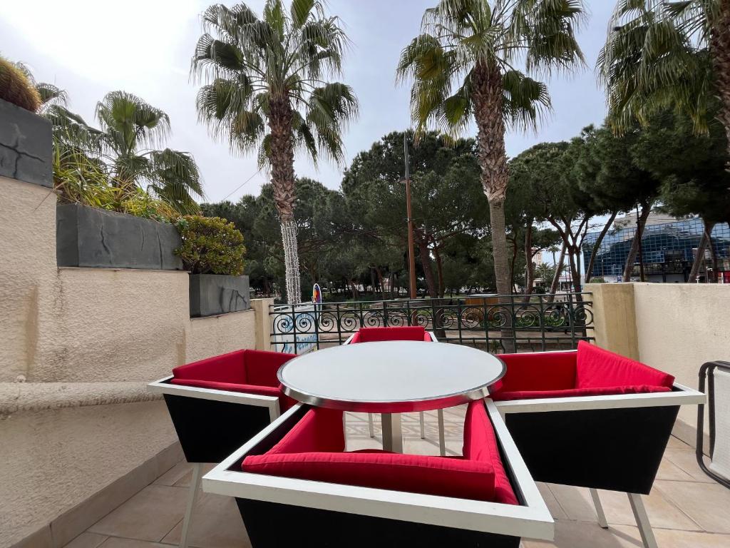 une table et des chaises rouges sur un balcon avec des palmiers dans l'établissement Appartement sur la Pinède à Juan les pins, à Antibes
